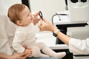 A doctor uses a magnifying glass to examine a baby's eye while the baby's parent holds them.