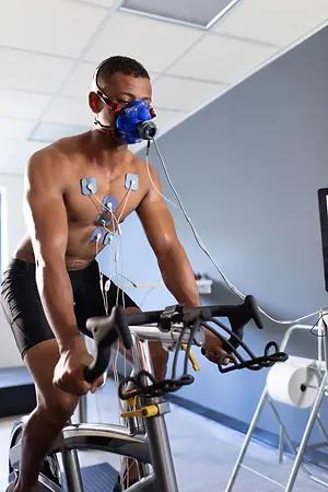 Man wearing a breathing mask and heart monitor electrodes while exercising on a stationary bicycle