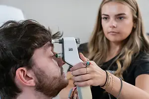 A woman is using an icare device to examine a man's eyes at the hospital.