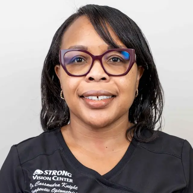 Portrait of a woman in glasses and a black shirt with the text 'Strong Vision Center' on it, smiling at the camera
