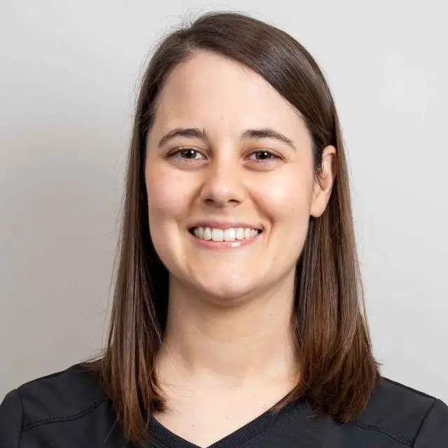 Headshot of a smiling woman with brown hair in a black shirt.