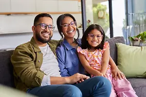 A man, woman, and young girl are sitting on a couch in a living room, smiling and posing for a photo.