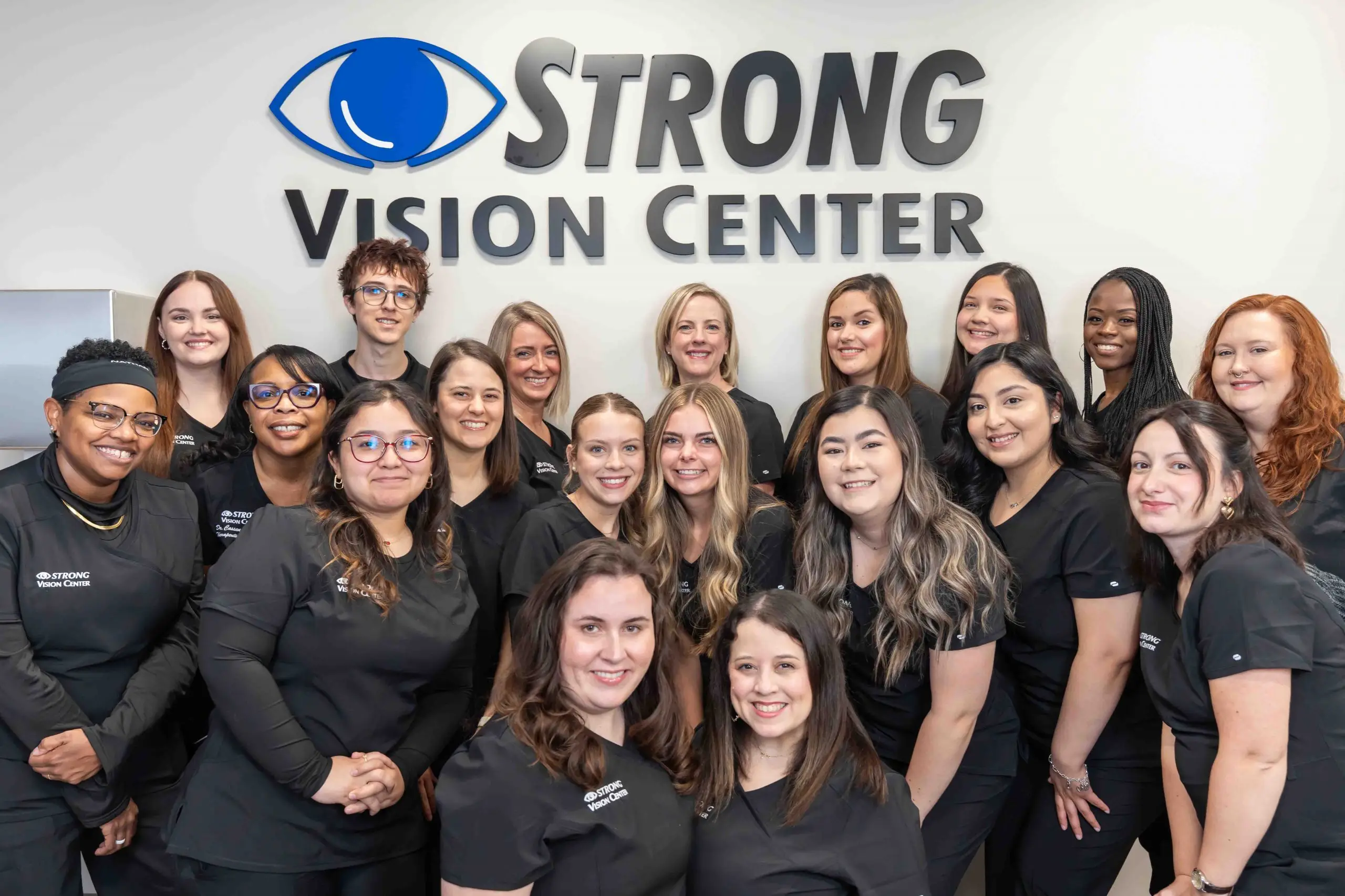 Group of women and men in black uniforms posing for a photo in front of the Strong Vision Center logo