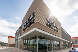 An exterior view of the Strong Vision Center in Fort Worth, Texas, with cars parked in front and a cloudy sky in the background.