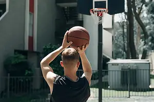 A man is holding a basketball above his head and seems to be playing in the backyard.