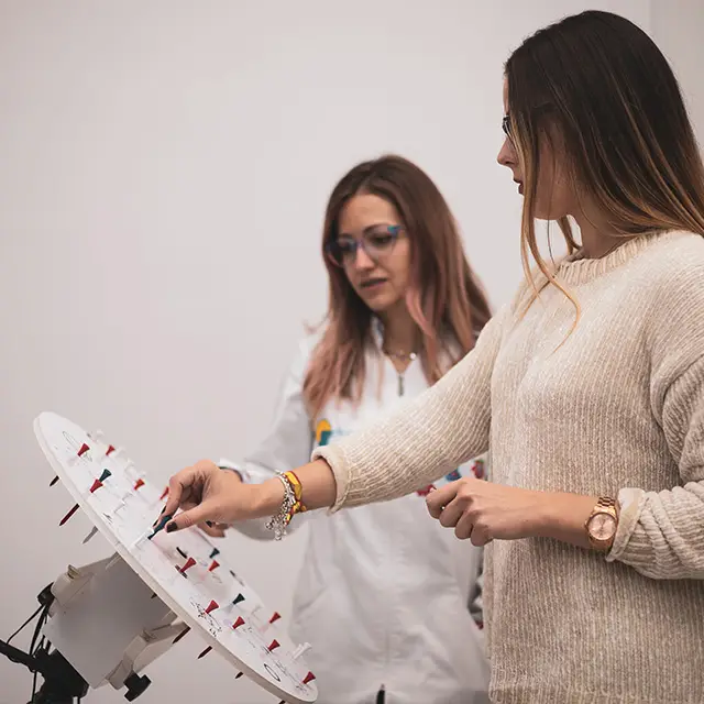 Two women standing in front of a white object with red pins