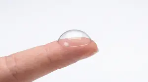 A fingertip with a clear contact lens on it, set against a white background