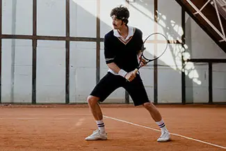 A man is standing on a tennis court holding a tennis racket with a serious expression on his face