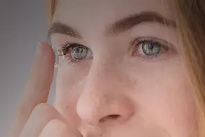 Close up of a woman holding a contact lens and placing it in her eye