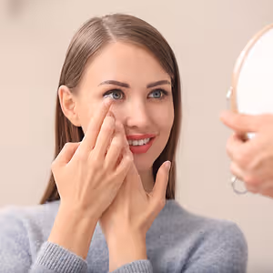 A woman puts in a contact lens in front of a mirror.