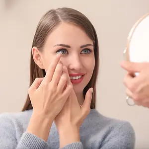 A woman puts in a contact lens in front of a mirror.