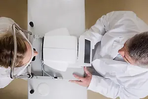 An optometrist is examining a patient's eyes with a slit lamp in a clinic.