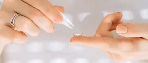 A woman is putting on a contact lens with a pair of tweezers.