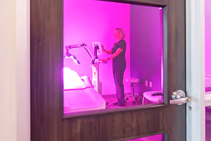 A woman is standing in front of a machine in a room with pink lighting.
