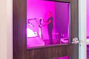 A woman is standing in front of a machine in a room with pink lighting.