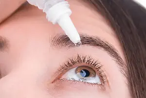 Close-up of a woman's face with a droplet of eye drops being applied to her eye