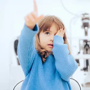 little girl in a blue sweater covering her eyes with her hands at the optometrist's office