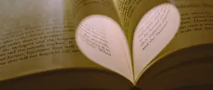A book is open to a page with text about a scientific presentation, and a heart shape is formed by the way the book is opened, with a warm, golden light illuminating the inside of the book.