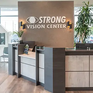 A modern reception area for a vision center with a wooden desk, glass top, and a sign reading 'STRONG VISION CENTER'.