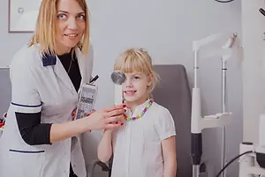 A female doctor checks the eyes of a young girl with an eye chart in a medical office.