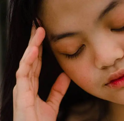 Close up of a woman with her eyes closed and her hand on her head