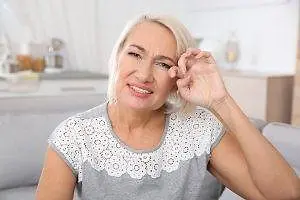A woman sitting on a couch and smiling with her hand on her face.
