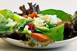 A plate with a salad with apple, carrot, tomato, and lettuce, with white cheese in between