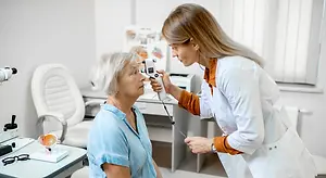 An elderly woman undergoing an eye examination by a female doctor in a medical setting.