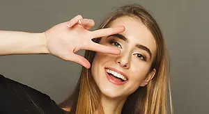 woman in black top with hand on forehead making peace sign