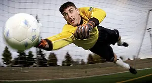 Soccer player in yellow jersey catches a ball in the air in front of a goal net