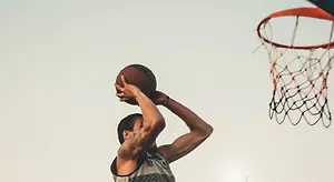 A basketball player is practicing by shooting a basketball into a basketball hoop.