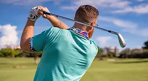 A man with a beard and glasses is playing golf on a sunny day