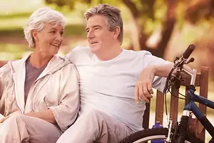 A smiling senior couple sits on a bench with a bike between them
