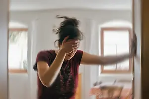 A woman in a room with her hands on her head and her body slightly blurred.