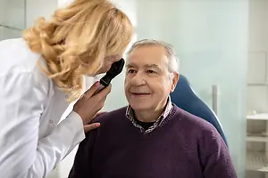 a woman doctor examining a senior man's eyes with an ophthalmoscope