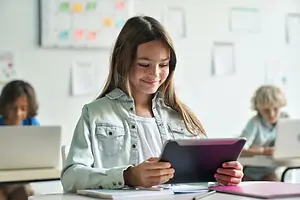 A girl is smiling while looking at her tablet in a classroom