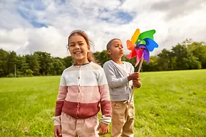 Two children playing in a grassy field with a colorful pinwheel