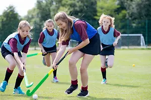 Four girls playing field hockey on a grassy field with trees in the background