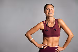 A smiling woman in workout clothes poses with her hands on her hips