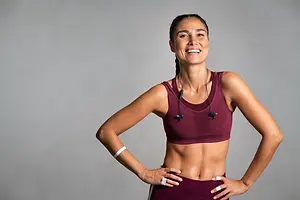 A smiling woman in workout clothes poses with her hands on her hips