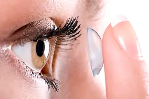 A woman is touching her eye with her finger while wearing a contact lens