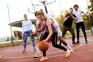 A group of people playing basketball on an outdoor basketball court with one woman holding a basketball in her hand
