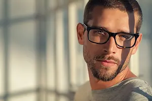A man with a beard and glasses standing in front of a window
