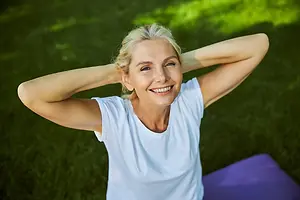 Smiling woman lying on grass with her hands behind her head