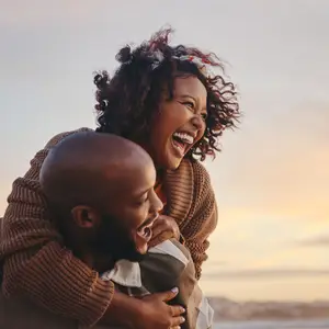 A man and woman smiling and laughing while the man is holding the woman from behind