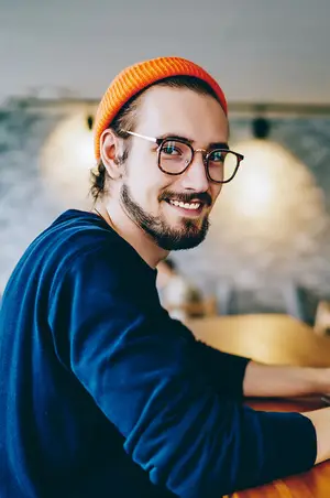 A smiling man with glasses and a beanie is sitting in a restaurant