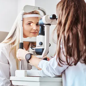 A woman is getting her eyes checked by another woman in a white lab coat.