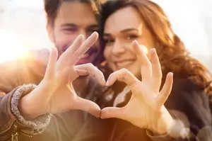 Couple forming a heart shape with their hands and smiling at the camera.