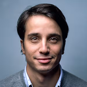 man smiling and wearing a gray sweater and blue shirt
