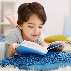 A young girl is lying on the floor, smiling, and reading a book.